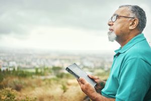 Bible, praying or senior man in nature for praise, hope or Christian religion with holy mindfulness